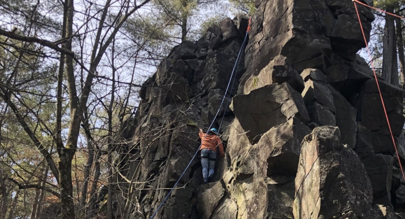 A person wearing safety gear is secured by ropes as they climb up a rock formation.